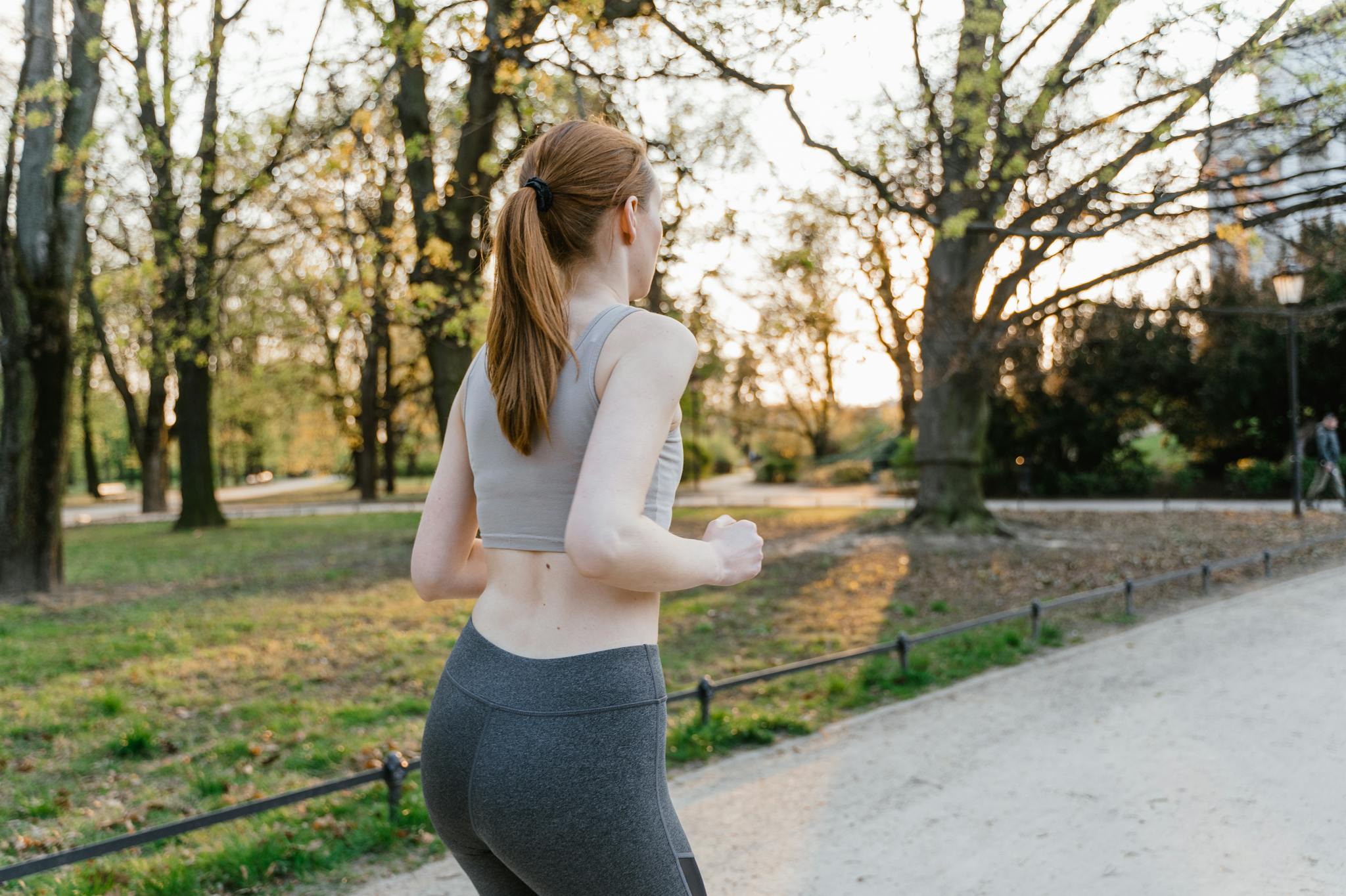 A woman jogs in a park during sunset, enjoying an outdoor fitness routine.