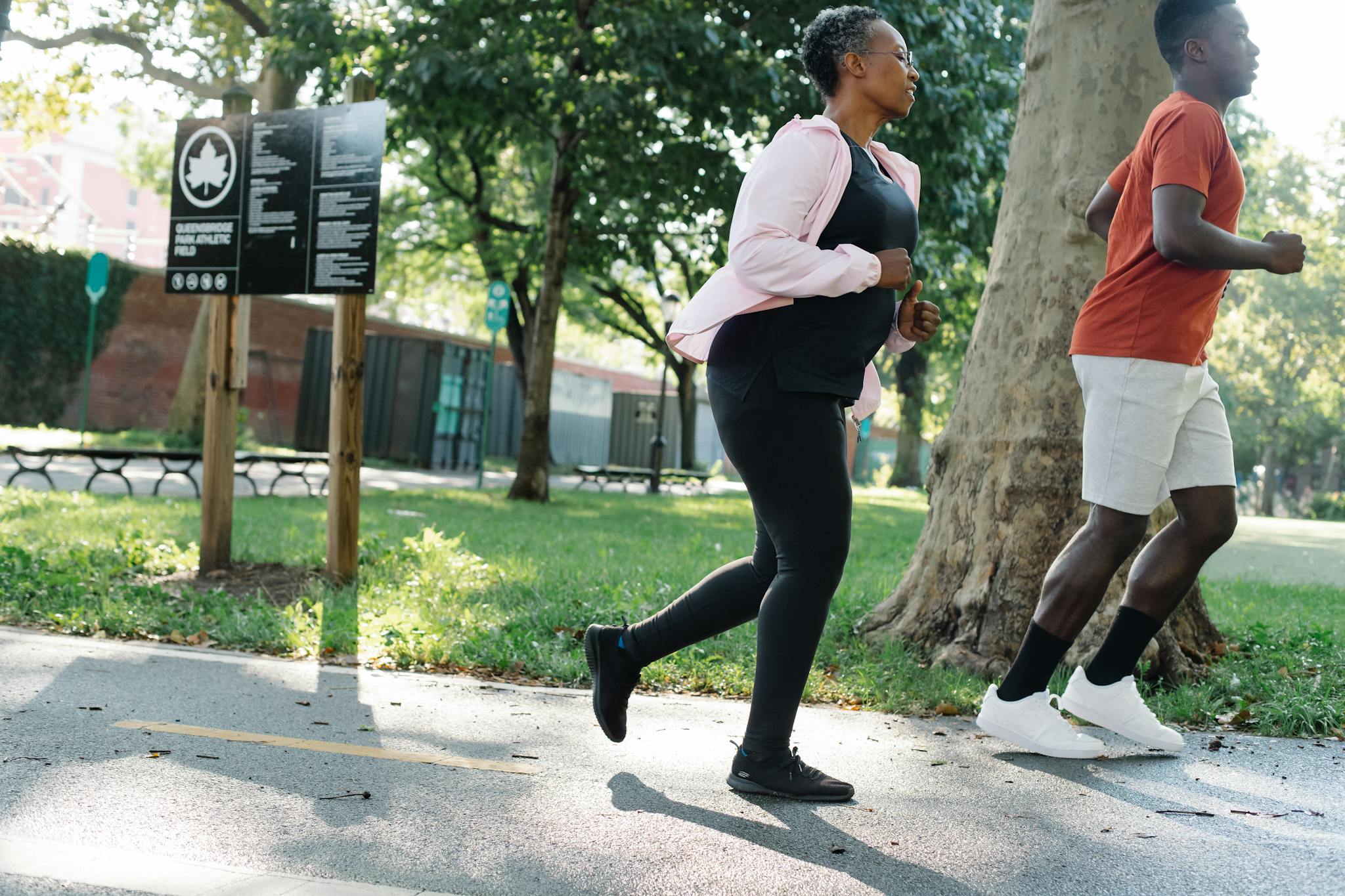 Two adults jogging on a sunny day in a green park, promoting fitness.